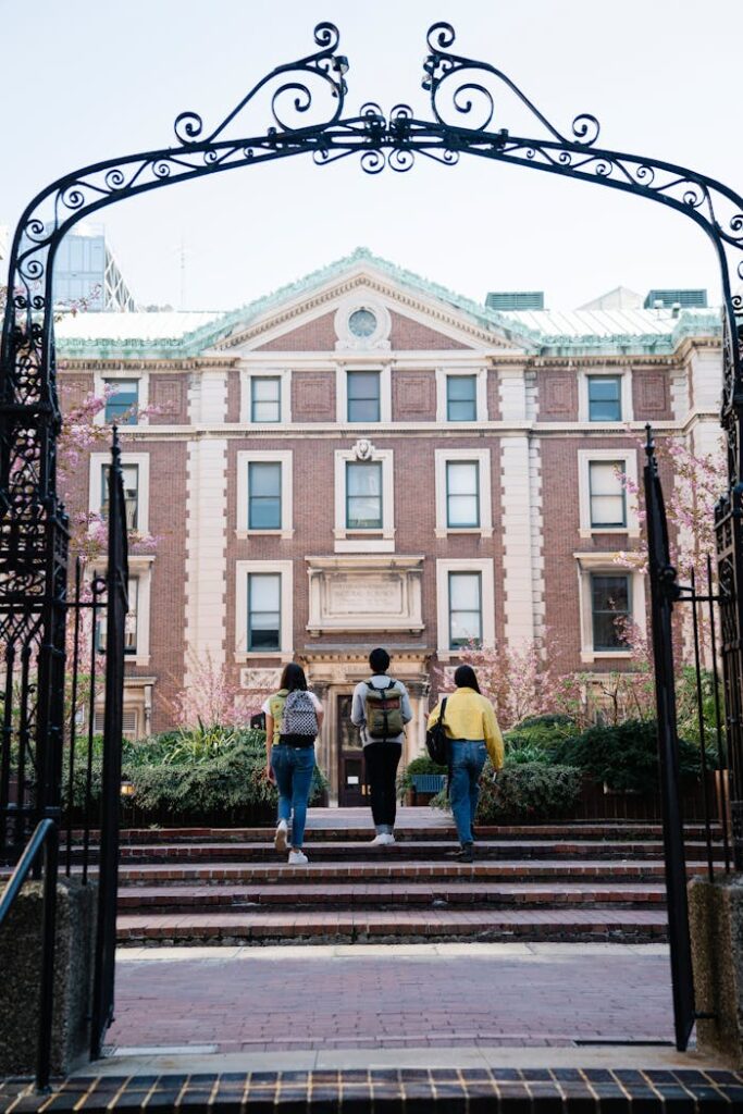 Three students walk through an archway towards a historic university building on campus.